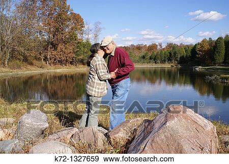 Loveing elderly couple embracing by lake View Large Photo Image Stock Photo - Loveing elderly couple embracing by lake. Fotosearch