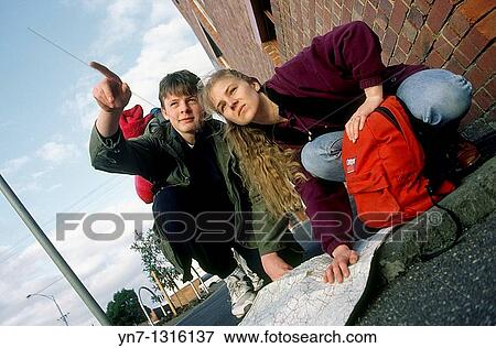 Stock Photo - low angle view of couple of backpackers in street reading their map. Fotosearch