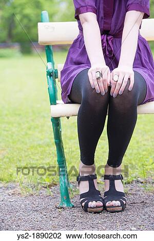 Lower section of woman sitting on bench in a park View Large Photo Image Stock Image - Lower section of woman sitting on bench in a park. Fotosearch