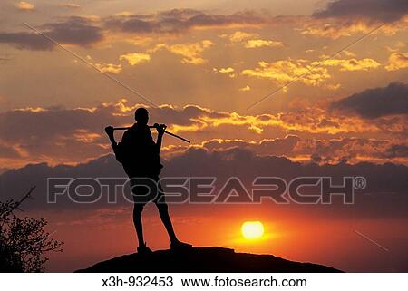 Stock Image - Maasai warrior standing up on hill at sunset, Namamga area, Kenya, East Africa. Fotosearch