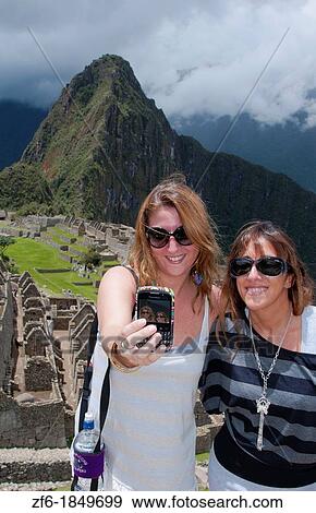 Machu Picchu famous ruins from above with two European tourists taking cell photo in Peru from Inca history View Large Photo Image Stock Photo - Machu Picchu famous ruins from above with two European tourists taking cell photo in Peru from Inca history. Fotosearch