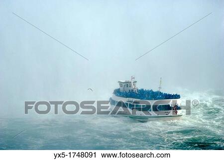 Stock Image - Maid of the Mist boat carrying tourists at the bottom of Niagara Falls. Fotosearch