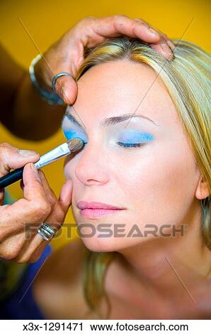 Stock Image - Makeup artist applying eyeshadow on a young woman with eyes closed. Fotosearch