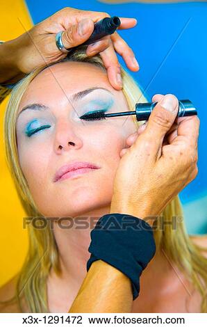 Stock Image - Makeup artist applying mascara on a young woman with eyes closed tilted face. Fotosearch