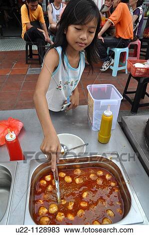 Stock Image - Malacca (Malaysia): a girl serving? fish balls? in a Chinatown's street stall. Fotosearch