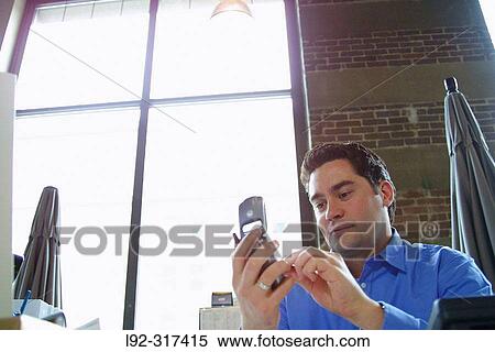 Male at desk with cell phone View Large Photo Image Stock Photography - Male at desk with cell phone. Fotosearch