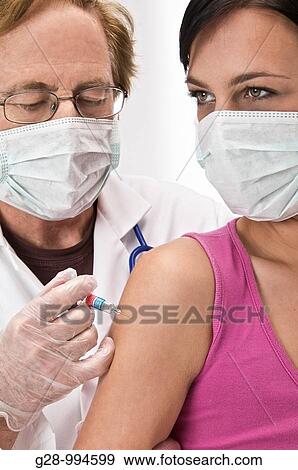 Stock Photo - male doctor with mask vaccinating or giving an injection to a young woman patient with mask too. Fotosearch