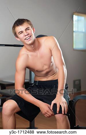 Male teenager laughing while sitting on a workout bench at fitness room View Large Photo Image Stock Photo - Male teenager laughing while sitting on a workout bench at fitness room. Fotosearch