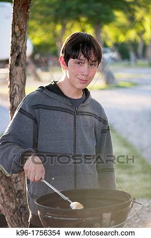 Picture - male teenager roasting a marshmallow in a campground. Fotosearch