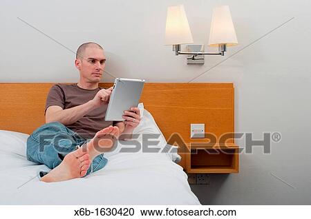 Stock Image - Man, 30-40 years, using digital tablet in a hotel room. Fotosearch