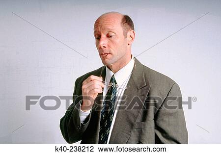Stock Image - Man, 40-45, holding glasses in mouth, with concerned look on face. Fotosearch
