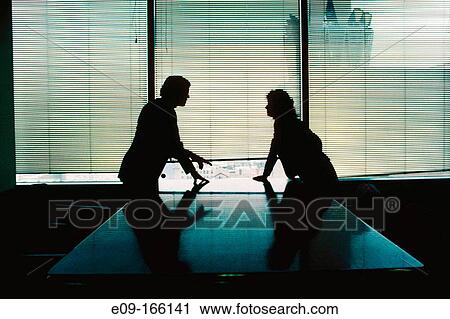 Man and woman in business attire, silhouetted, leaning on polished table from opposite sides, confronting each other, in conference room, with window behind View Large Photo Image Stock Image - Man and woman in business attire, silhouetted, leaning on polished table from opposite sides, confronting each other, in conference room, with window behind. Fotosearch