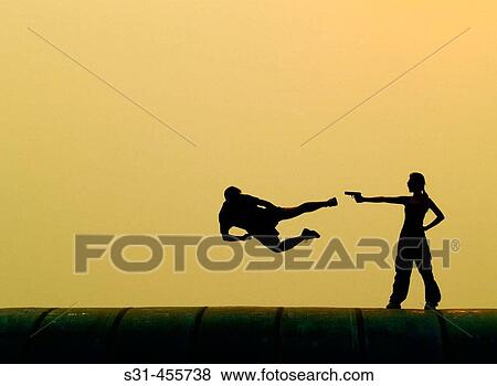 Man attacking with a flying kick to a woman who is pointing a gun to the man, man is caught in mid air View Large Photo Image Stock Photo - Man attacking with a flying kick to a woman who is pointing a gun to the man, man is caught in mid air. Fotosearch