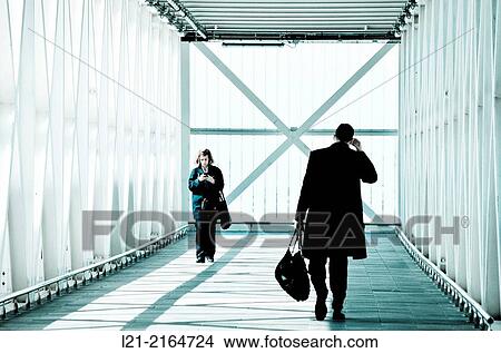 Picture - Man back with his bag talking with his mobile. Woman, holding her bags, using her smartphone with both hands. Catwalk, gangway, airport. El Prat de Llobregat, Barcelona, Catalonia, Spain.. Fotosearch