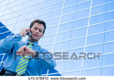 Stock Image - Man checking the time while on cell phone. Fotosearch