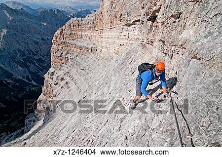 Man climbing the Giovanni Lipella via ferrata on Tofana De Rozes in the Dolomite Mountains near the city of Cortina in northern Italy View Large Photo Image Picture - Man climbing the Giovanni Lipella via ferrata on Tofana De Rozes in the Dolomite Mountains near the city of Cortina in northern Italy. Fotosearch