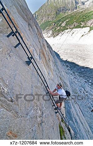 Picture - Man climbs a steel ladder via ferrata on the Mer de Glace Glacier near Montenvers high above the city of Chamonix France. Fotosearch