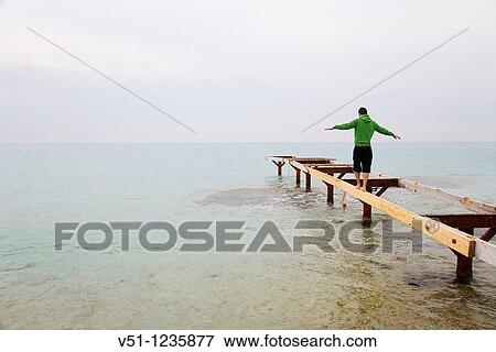 Stock Photo - Man doing balance in a pier in Formentera. Fotosearch