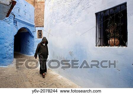 Picture - Man dressed traditionally walking in a street in the Chefchaouen Old Town Medina, Morocco.. Fotosearch