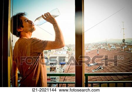 Man, drinking water from a plastic bottle, on a balcony. In the background, a cityscape. View Large Photo Image Picture - Man, drinking water from a plastic bottle, on a balcony. In the background, a cityscape.. Fotosearch