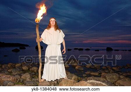 Stock Photo - Man Fire Dancer in White Costume Holding Torch by Water. Fotosearch