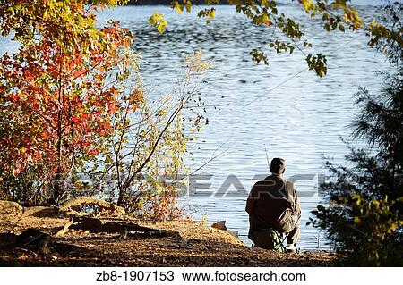 Stock Image - Man fishing from the shore of a lake, North Carolina, USA. Fotosearch