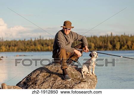 Stock Image - Man fishing with his dogin Paksuniemi in Swedish lapland. Fotosearch