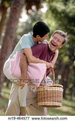 Stock Photo - man gives a woman a piggy back ride to a picnic. Fotosearch