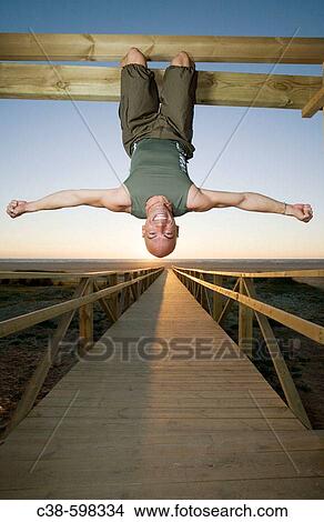 Picture - Man Hanging Up Side Down on Footbridge. Fotosearch