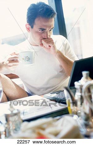 Man having breakfast and looking at laptop in a hotel room View Large Photo Image Stock Photo - Man having breakfast and looking at laptop in a hotel room. Fotosearch