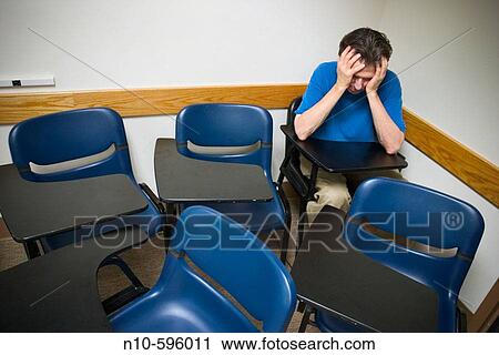 Man, holding onto his head with his hands, sitting in his student desk in an otherwise empty college classroom. View Large Photo Image Stock Image - Man, holding onto his head with his hands, sitting in his student desk in an otherwise empty college classroom.. Fotosearch