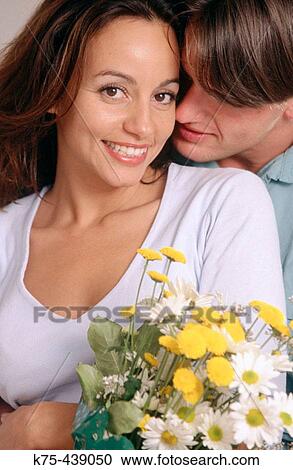 Stock Image - Man hugs girlfriend with bouquet of flowers. Fotosearch