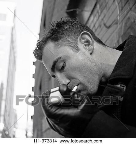 Picture - Man in alley; lighting a cigarette. Fotosearch