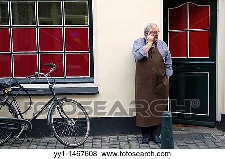 Man in apron making a phone call outside his shop. View Large Photo Image Stock Photo - Man in apron making a phone call outside his shop.. Fotosearch