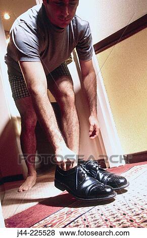 Stock Photo - Man in boxers picking up polished shoes from hotel room door. Fotosearch