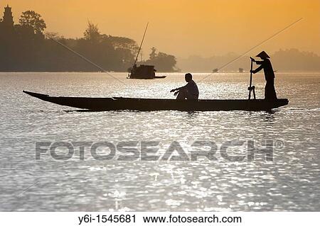 Stock Image - Man in conical hat ferries passenger across Song Huong Perfume River Hue central Vietnam. Fotosearch