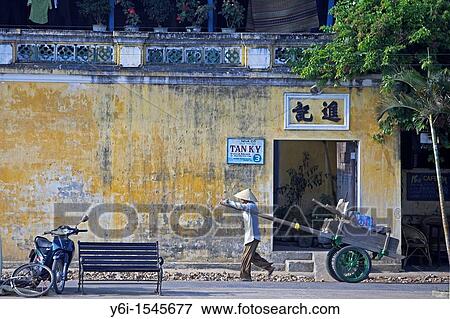 Stock Photo - Man in conical hat pulls hand cart along street Hoi An historic town mid Vietnam. Fotosearch