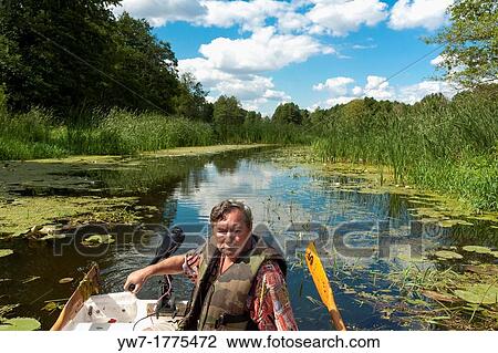 Stock Image - Man in fishing boat on Narew river, Poland. Fotosearch