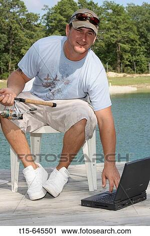 Stock Image - man in his 30's fishing and checking stocks, emails on his laptop looking happy. Fotosearch