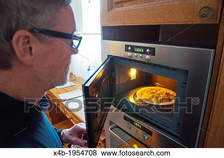 Stock Photo - Man in his 70s heating a meal with microwave oven at home Pori Finland Europe.. Fotosearch