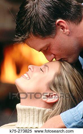 Stock Photography - Man kisses woman in front of fireplace. Fotosearch