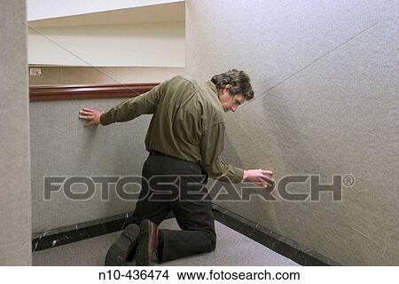 Man kneeling against a wall in an office building. View Large Photo Image Picture - Man kneeling against a wall in an office building.. Fotosearch