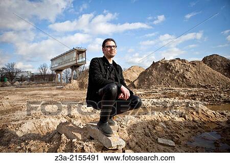 Stock Image - Man kneeling in landscape with Strijp-R gangway in the background.. Fotosearch