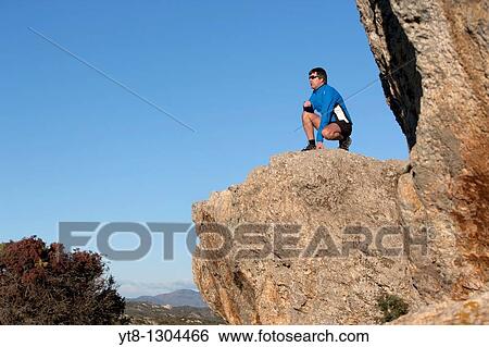 Man kneeling on a rock ledge View Large Photo Image Stock Photograph - Man kneeling on a rock ledge. Fotosearch
