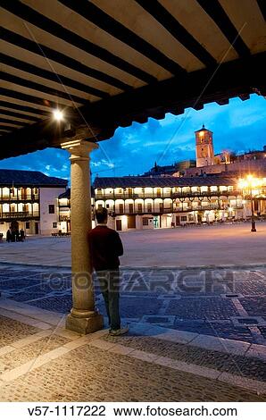 Stock Image - Man leant against a column looking at the Main Square, night view. Chinch? n, Madrid province, Spain.. Fotosearch