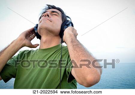 Picture - Man listening to music with headphones near the sea.. Fotosearch