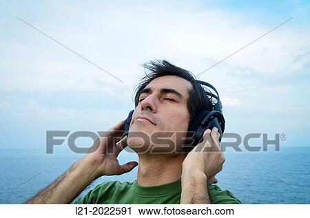 Stock Image - Man listening to music with headphones near the sea.. Fotosearch