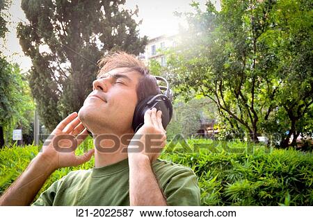 Man listening to music with headphones in public garden. View Large Photo Image Stock Photo - Man listening to music with headphones in public garden.. Fotosearch