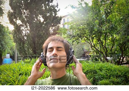 Stock Photograph - Man listening to music with headphones in public garden.. Fotosearch