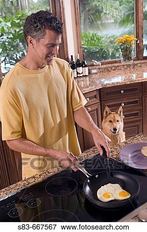Stock Photo - Man making eggs in kitchen with dog watching. Fotosearch
